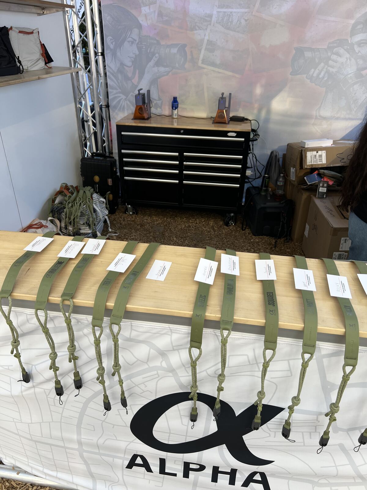 Row of custom embroidered canvas tote bags with army green carrying straps displayed on a wooden shelf